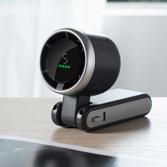 Black foldable fan with LED display placed on wooden desk surface.