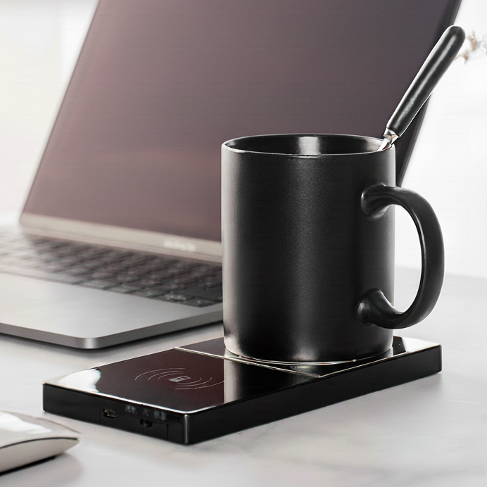 Mug sitting on smart mug warmer beside a laptop on a desk.