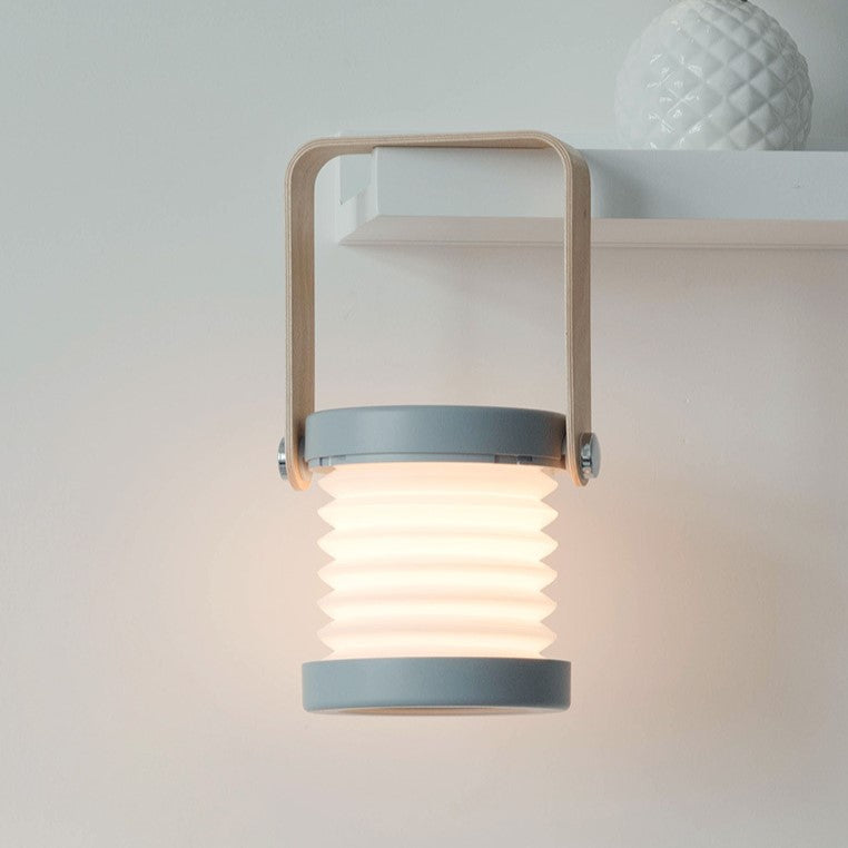 Grey color variant of collapsible lantern displayed on shelf emitting soft light.