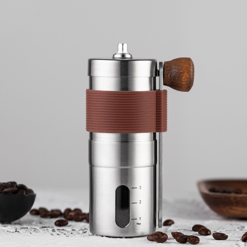 Compact coffee grinder standing on table beside scattered coffee beans.